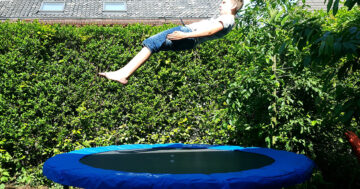 Junge springt auf blauem Trampolin im Garten